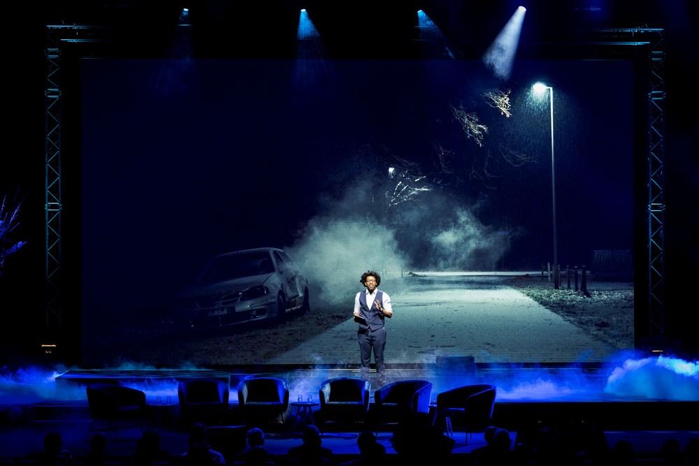 Terrance alone on a large stage in front of a foggy night-street backdrop