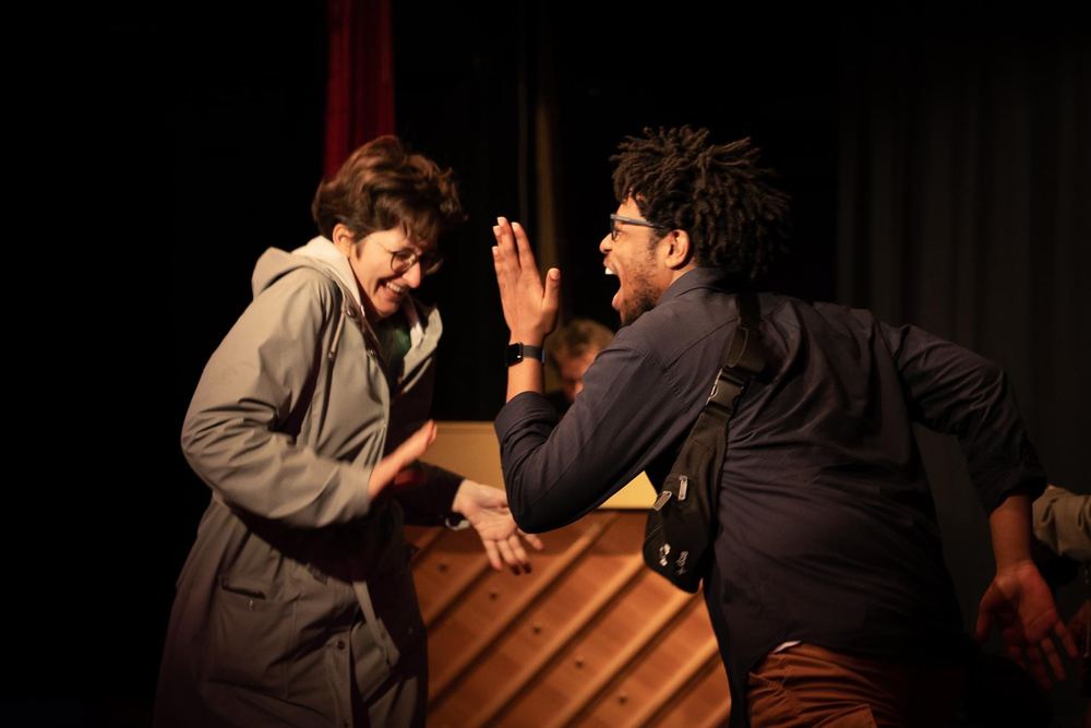 Terrance and a scene partner mid high-five on a dark stage