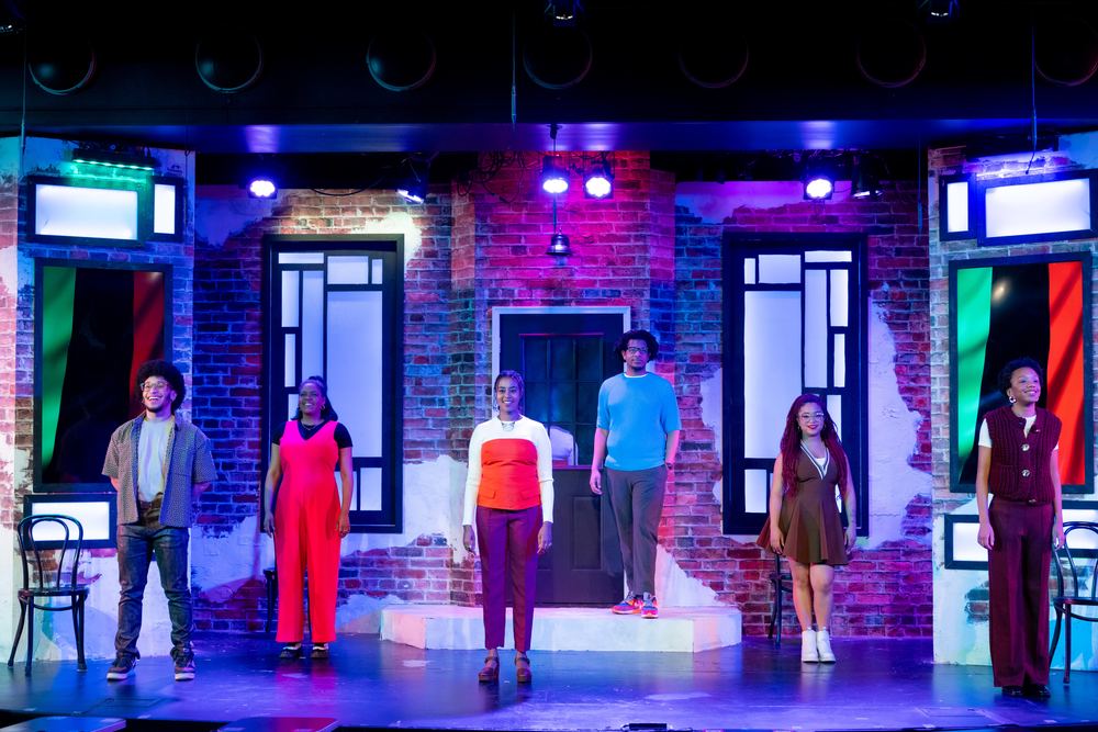 The cast of a Second City revue spread across a brick-walled stage set under purple light