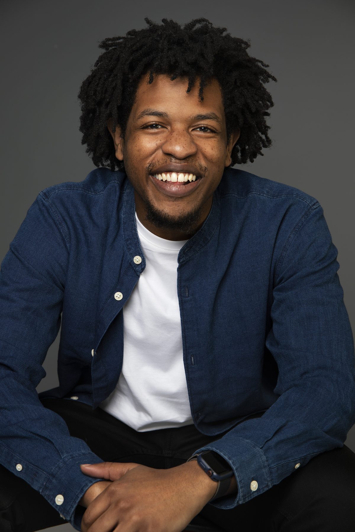 Portrait of Terrance Lamonte, Jr. laughing, wearing an open denim shirt over a white tee